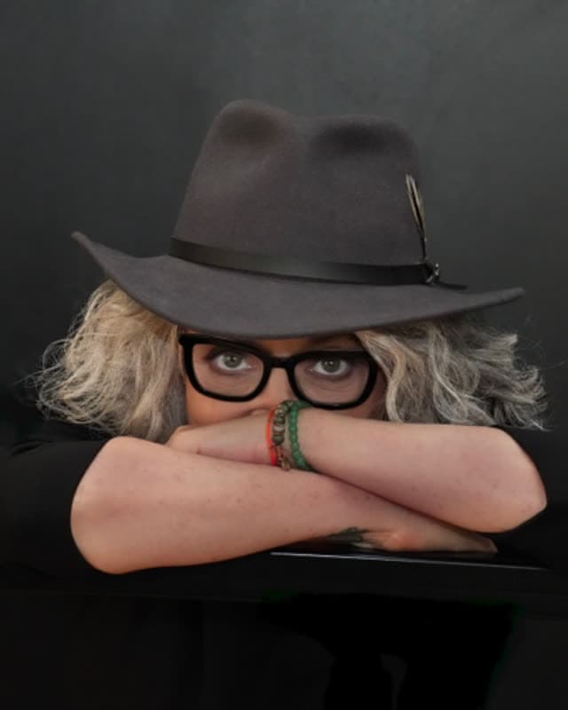Sheri Lynch in a fedora and glasses, arms folded